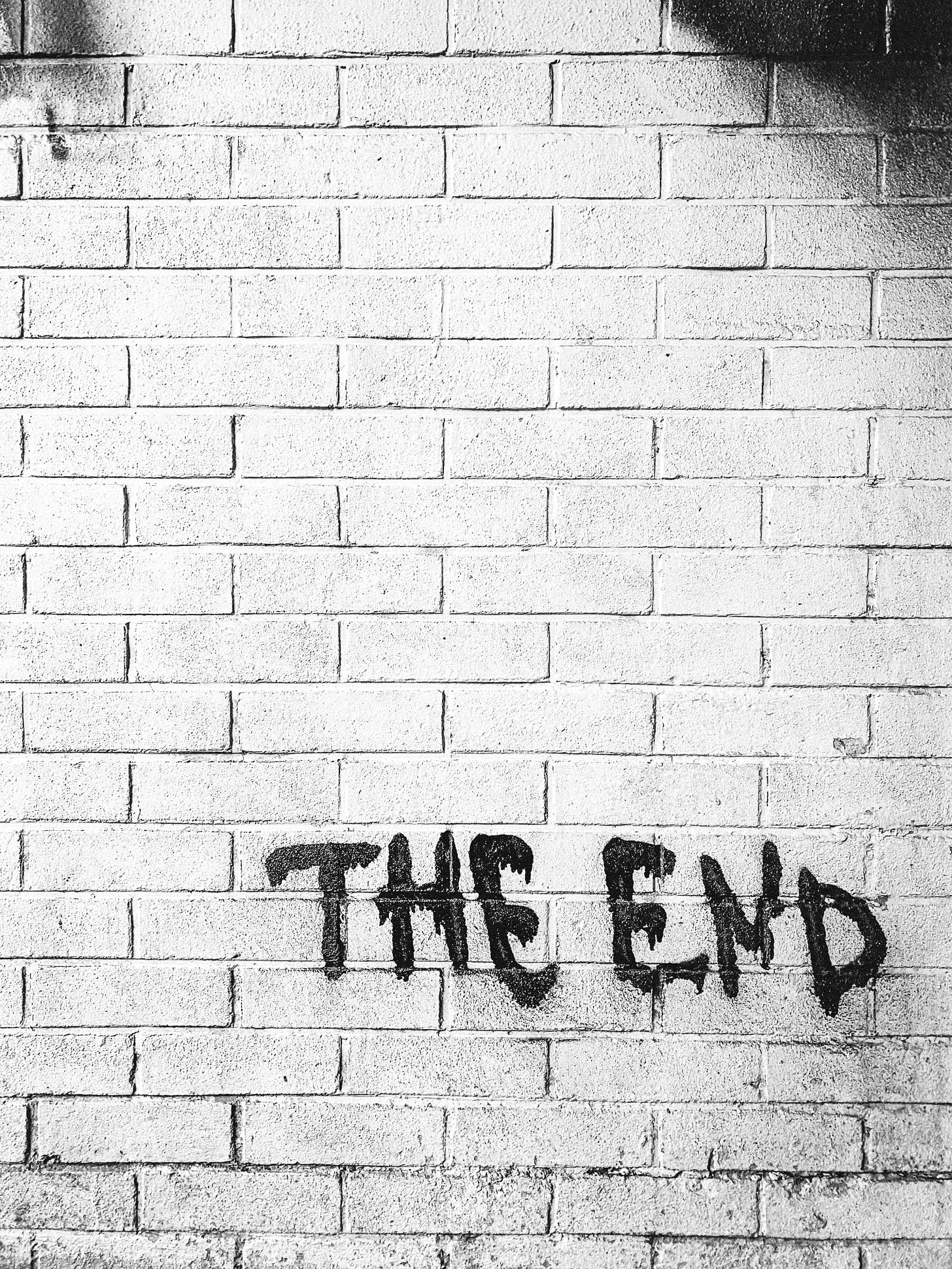 a black and white image of a brick wall which has the word The End spray painted on it a black and white image of a brick wall which has the word The End spray painted on it