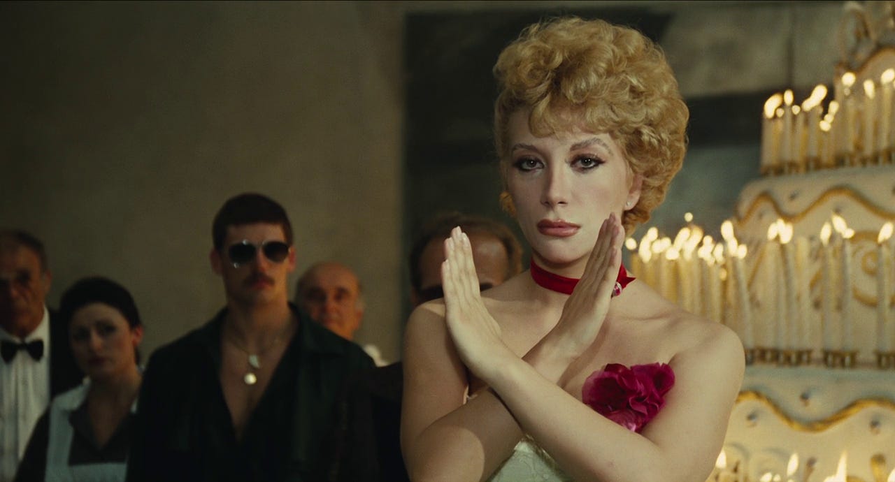 An obvious gay guy and a beautiful showgirl-style blonde stand before a gigantic cake in Fellini's "City of Women" (1980)
