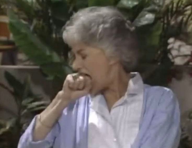 This may contain: an older woman is eating something in her hand while sitting on a chair with potted plants behind her