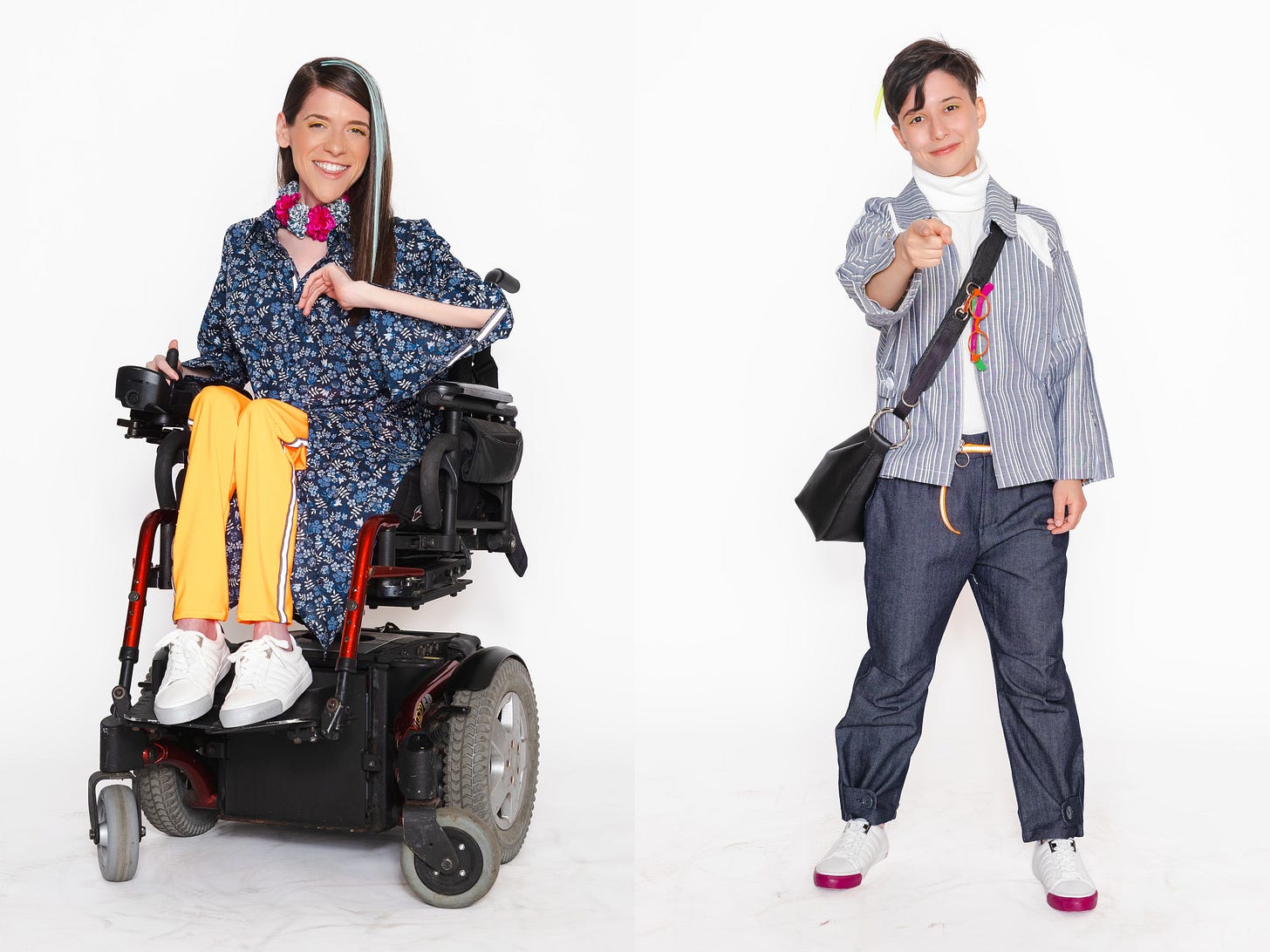 Two fashion portraits against a white background. The model on the left, seated in a powered wheelchair, wears a blue patterned top and vibrant yellow pants. The model on the right, who is standing, wears a striped shirt over a turtleneck and points engagingly at the camera.