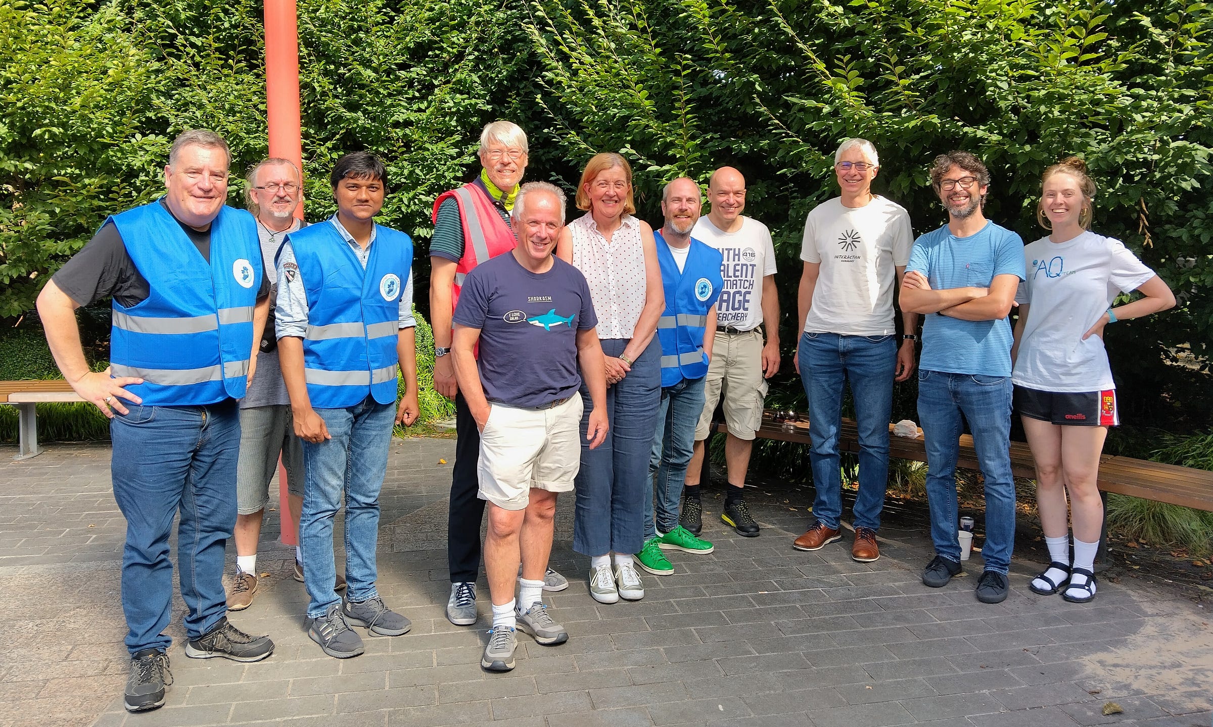 A group of about a dozen people standing in a park and smiling at the camera. A group of about a dozen people standing in a park and smiling at the camera.