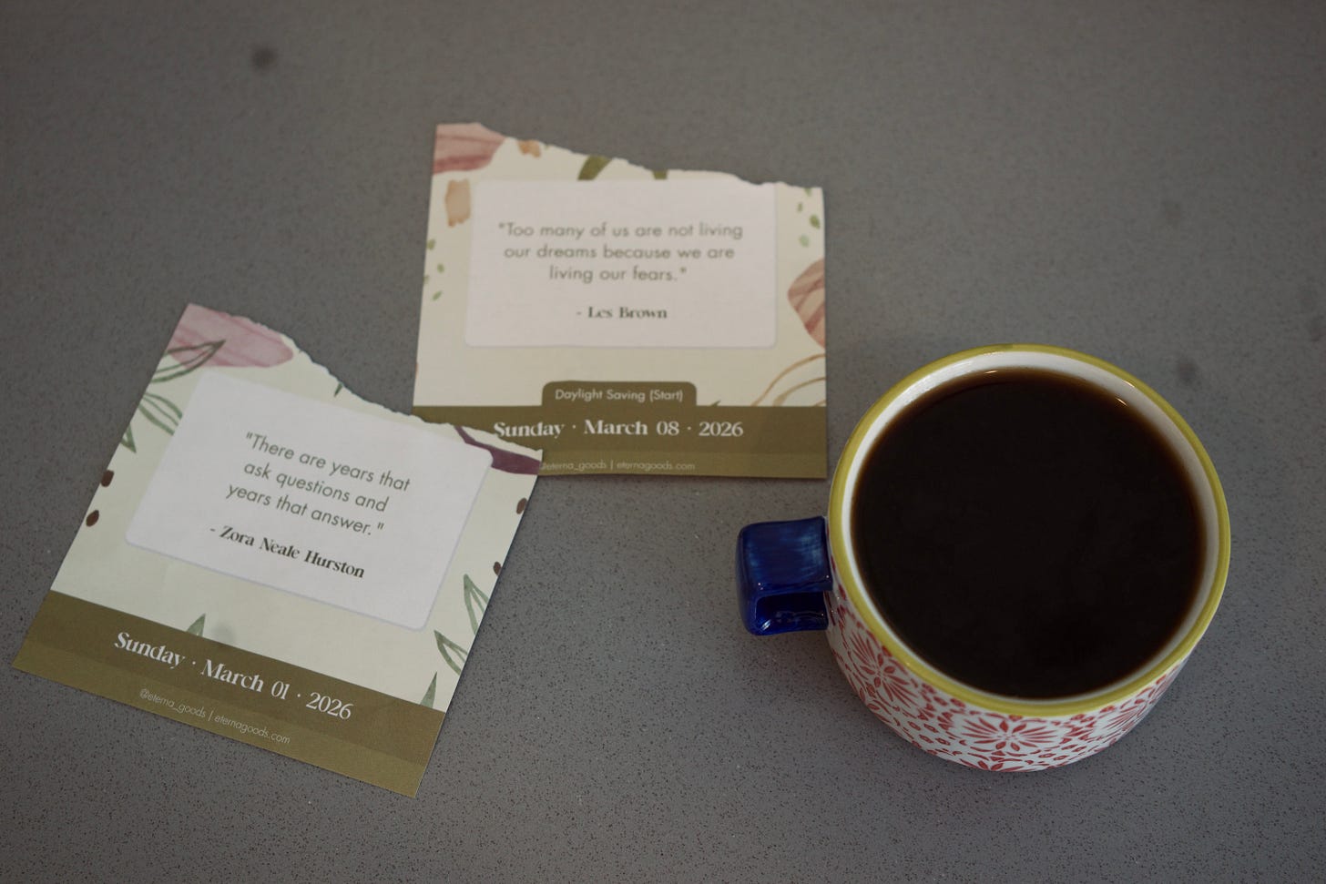Coffee cup beside two quote calendar cards on a tabletop, soft morning light, calm and reflective mood.