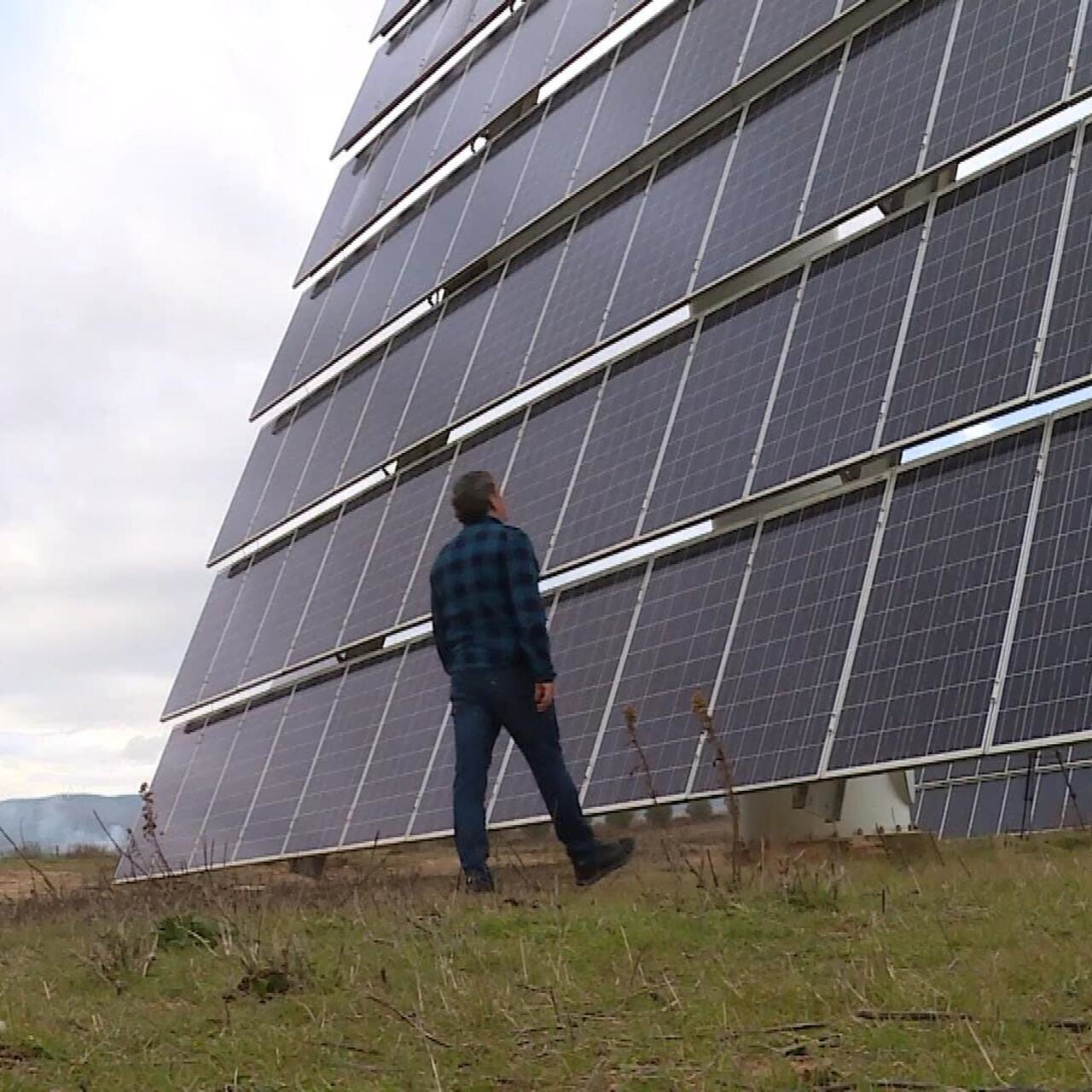 A person examines a large solar panel installation in a rural area, highlighting the solar energy context relevant to investment risks and crises in Spain
