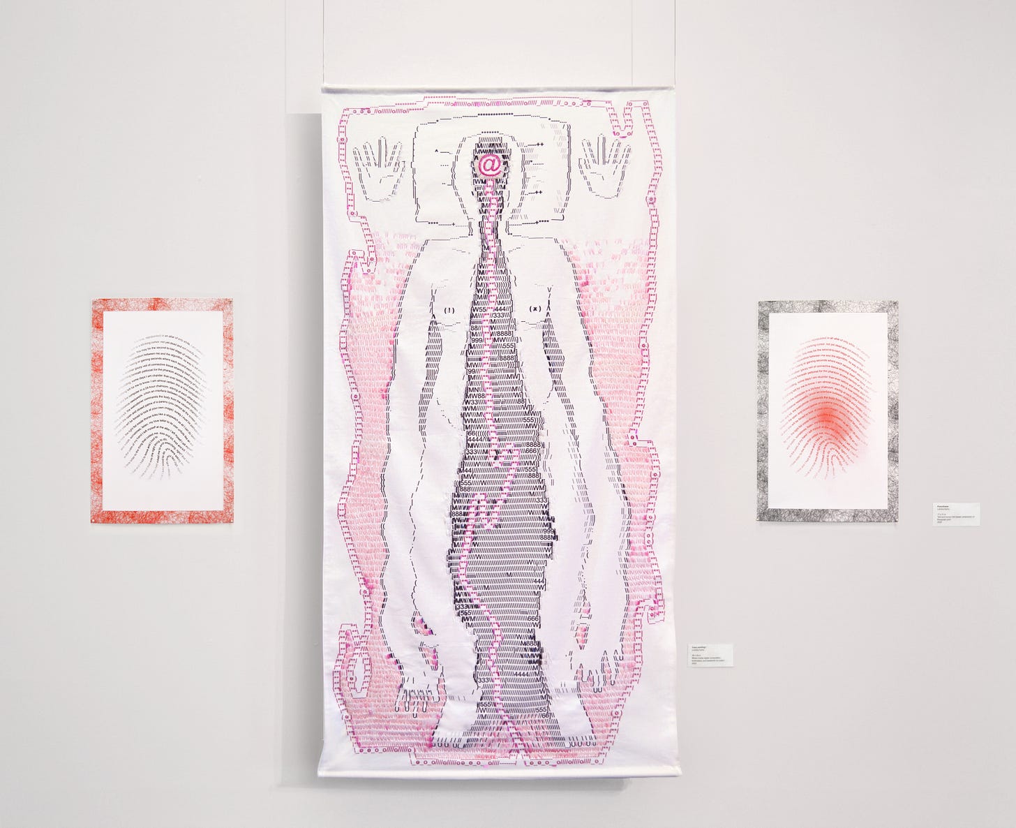 A triptych featuring a floating, white, cotton tapestry in the center, hanging by clear wire 2 inches from the wall, with two smaller risograph prints pinned on either side. Composed of printed black and magenta computer symbols with overlaid embroidery and beadwork, a humanoid figure laying on a pillow features a large gash resembling a cave or portal that opens from their forehead down to their limbs, which appear glued together. Inside the gash is a large “at” symbol, from which a magenta cord reminiscent of guts snakes down and out of the figure to surround it in a protective fashion. The two risograph prints feature the same poem composed in the shape of the artist’s right index finger print, printed inversely in black and red ink. The borders feature a pattern created by scanned clumps of their hair.