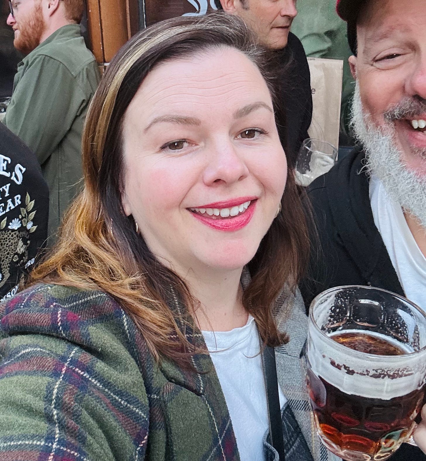 A selfie of Amber. She holds a beer and smiles into the camera. Half of David's face can be seen next to hers, but the rest is cropped out.