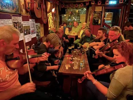 A lively Irish pub scene with musicians playing traditional Irish folk music. The setting is warm and inviting, with a group of people gathered around a wooden table, enjoying drinks and the vibrant atmosphere. Instruments like fiddles and guitars are prominently featured, contributing to the joyful ambiance. The pub is decorated with musical instruments and posters, enhancing the authentic Irish Craic experience.