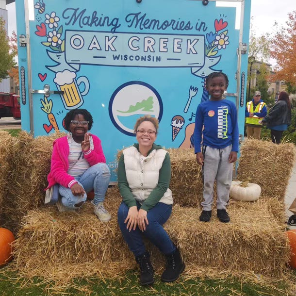 a woman and two young girls post on hay bales in front a sign about making memories in Oak Creek, Wisconsin