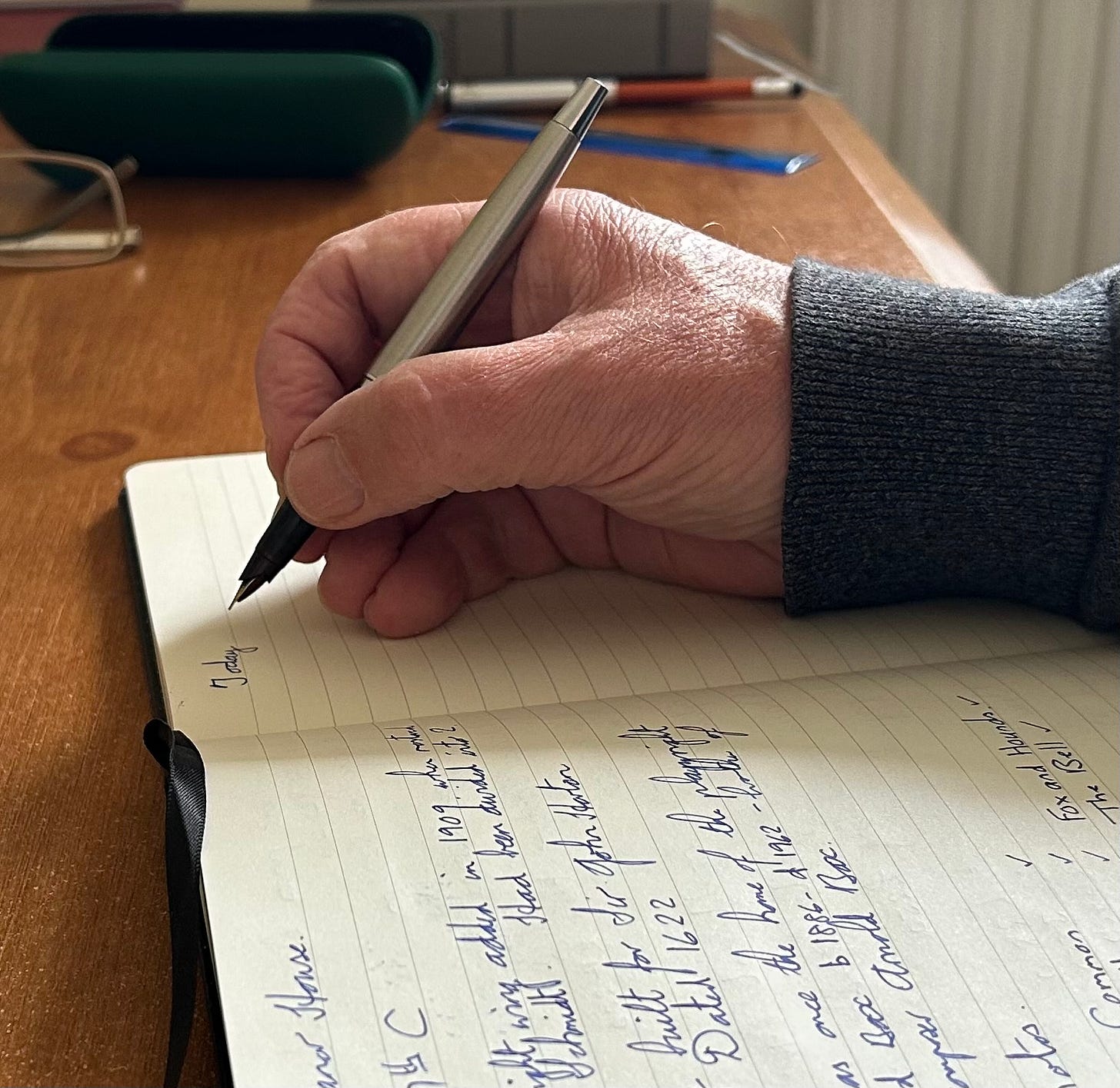 A hand holding a fountain pen writing on a notebook. 
