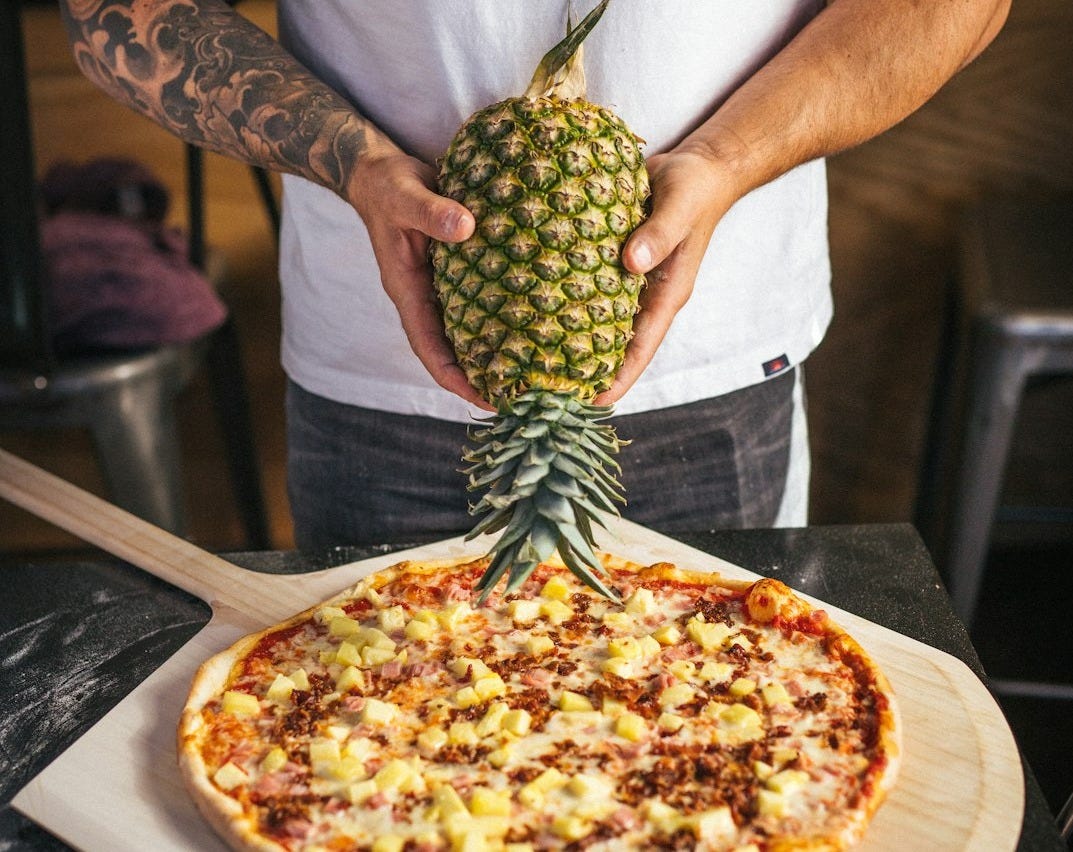a man holding a pineapple on top of a pizza a man holding a pineapple on top of a pizza