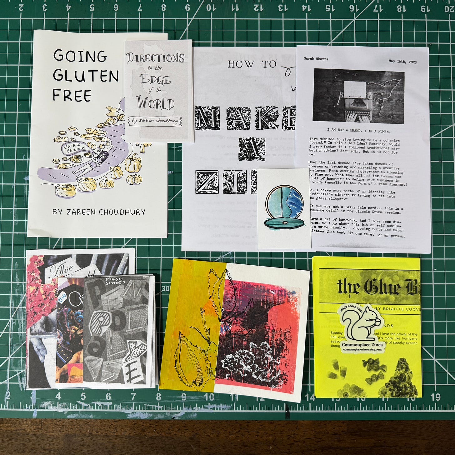 a photo of all the zines listed below, arranged on the green and white cutting mat on my desk.