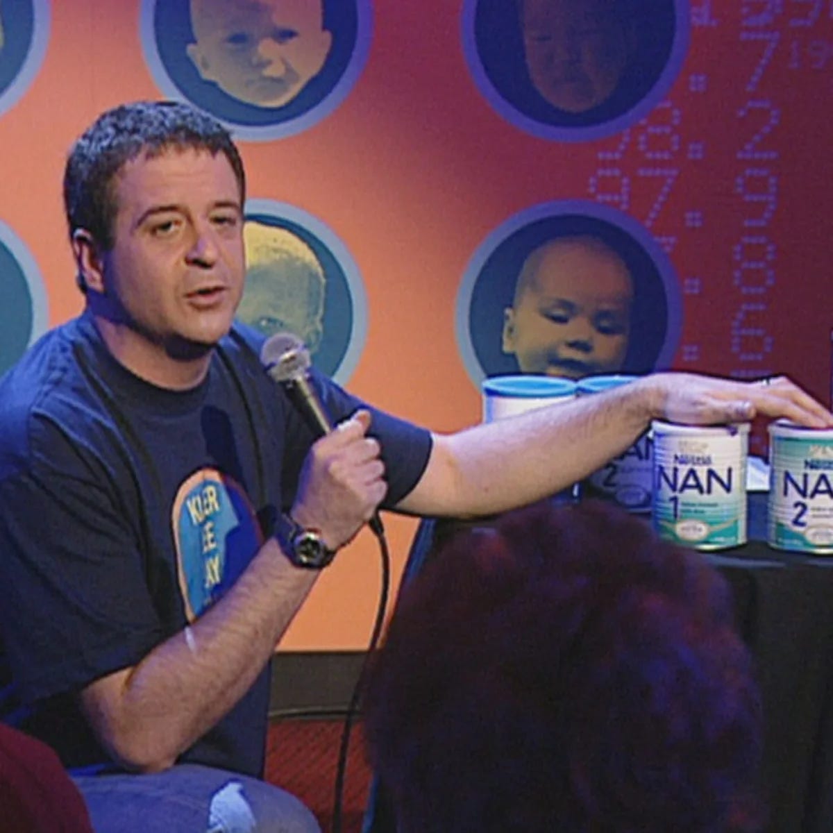 A young Mark Thomas on The Mark Thomas Comedy Product, his hand resting on cans of Nestle baby formula.