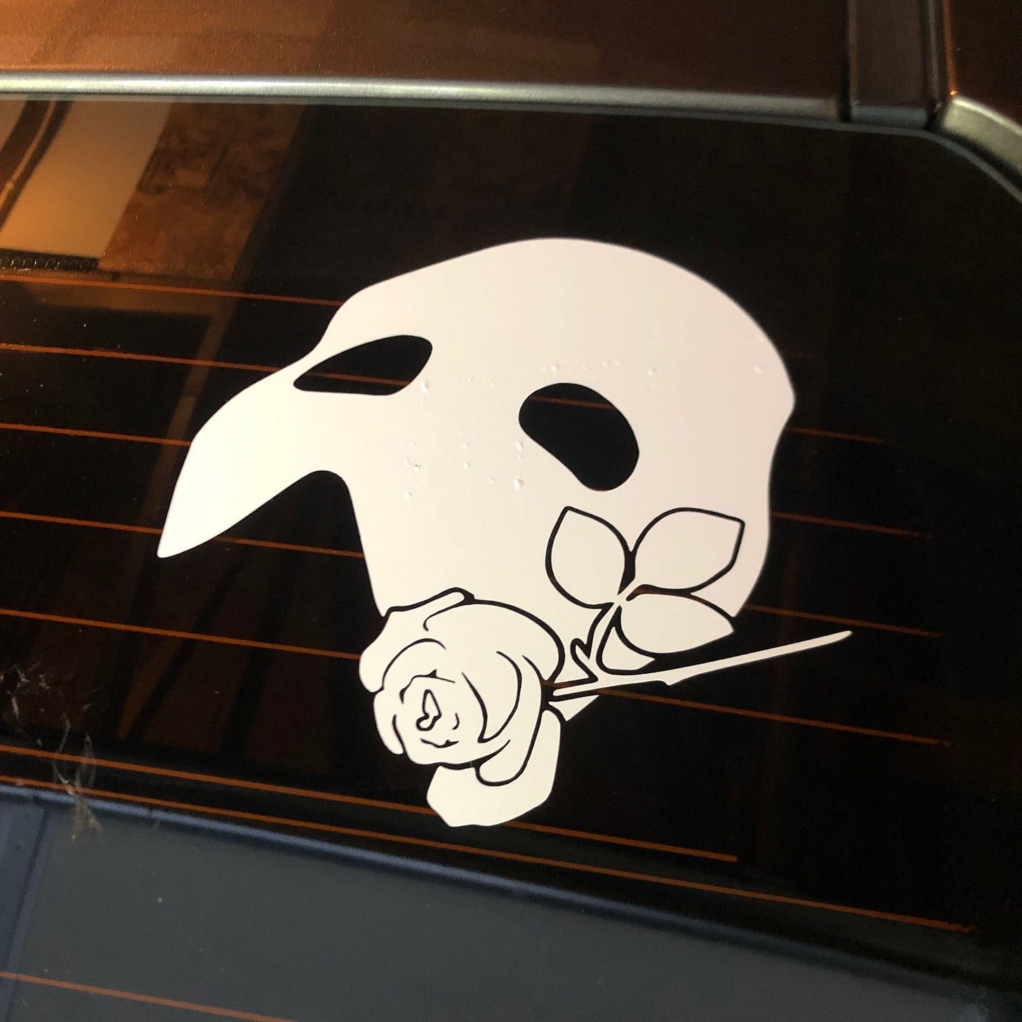 Vinyl car decal of a Phantom of the Opera mask with a rose beside it.