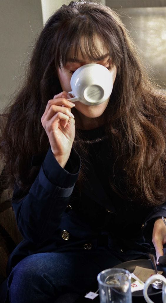 This may contain: a woman sitting on a couch drinking from a cup