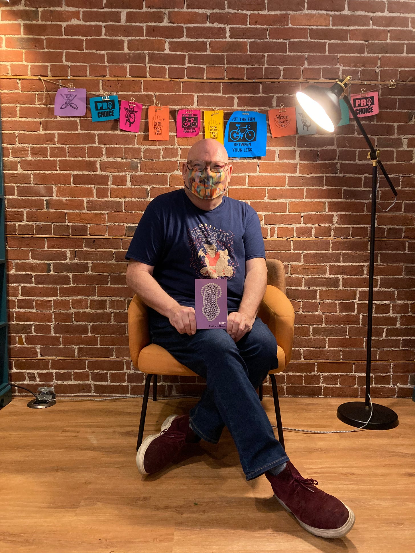 Kirby seated with their book "Poetry is Queer" at Venus Envy, Halifax