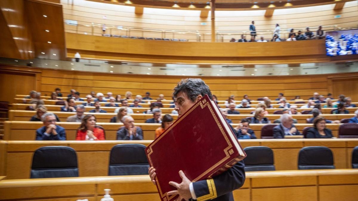 Un ujier del Senado retira la Constitución española del salón del pleno después del juramento de un nuevo senador.