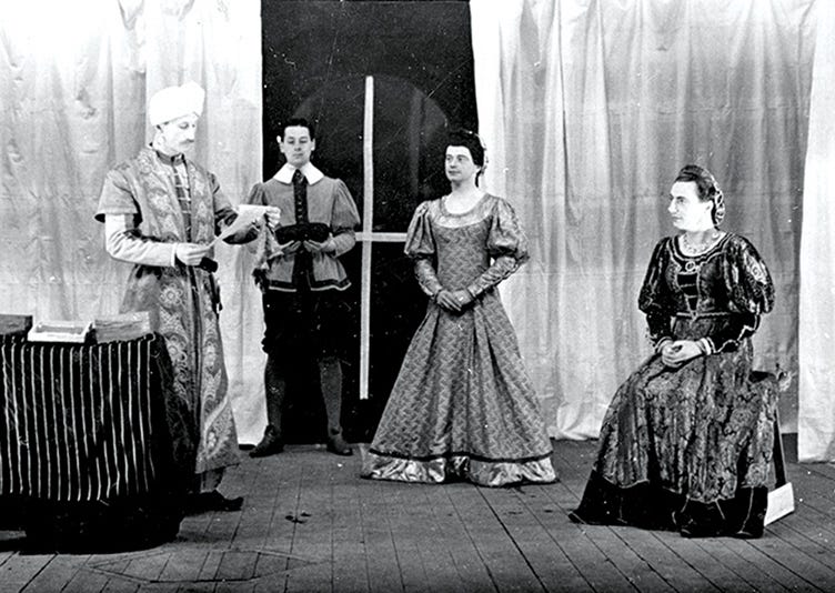 Actors on stage at Stalag Luft III, Poland, early 1940s. Imperial War Museum. One man wears a turban and presumably middle Eastern/Oriental/unspecified ‘exotic’ robes, while two female parts are played by men