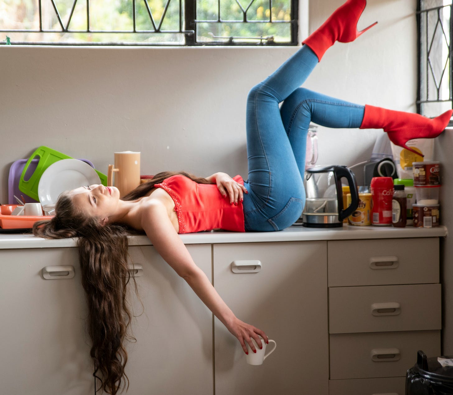 Woman lying across a kitchen counter with a relaxed expression, bathed in soft natural light during a quiet morning. Woman lying across a kitchen counter with a relaxed expression, bathed in soft natural light during a quiet morning.