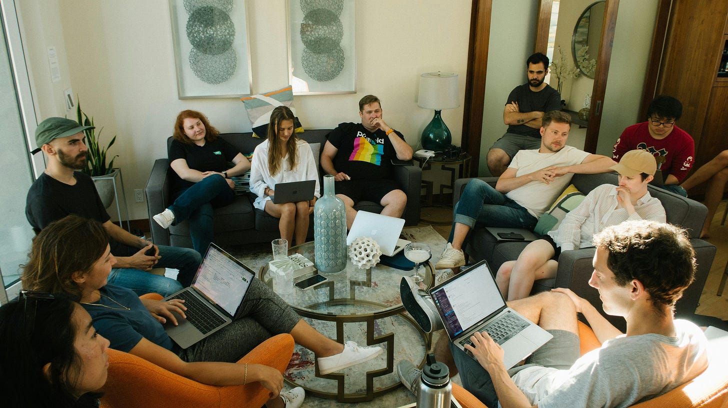 A group of journalists and media professionals working on laptops in a casual living room setting, sitting on couches around a coffee table, demonstrating the shift from institutional newsrooms to community-centered journalism. A group of journalists and media professionals working on laptops in a casual living room setting, sitting on couches around a coffee table, demonstrating the shift from institutional newsrooms to community-centered journalism.