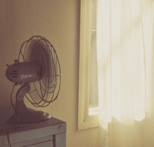 This may contain: an old fan sitting on top of a table next to a window with the sun shining through it