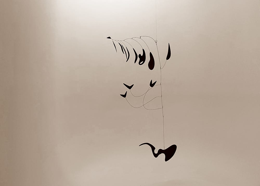 A black abstract metal mobile hangs almost hovering in a softly lit alcove. A black abstract metal mobile hangs almost hovering in a softly lit alcove.