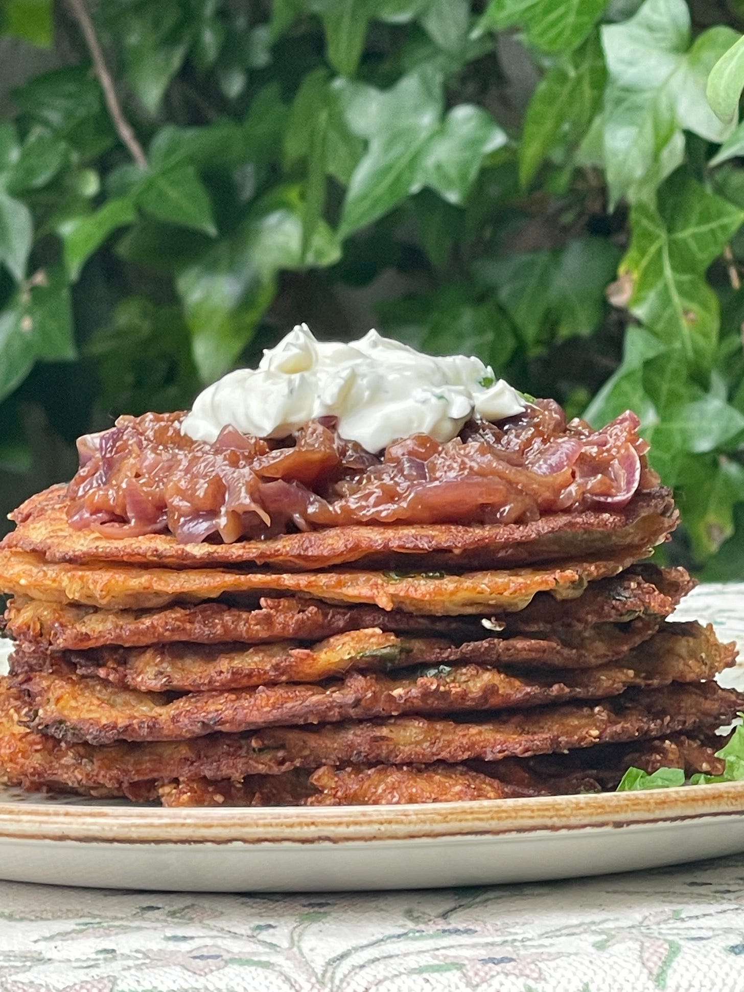 Golden-edged potato pancakes stacked high and crowned with jammy red onions and a dollop of cream, eaten outdoors. Golden-edged potato pancakes stacked high and crowned with jammy red onions and a dollop of cream, eaten outdoors.