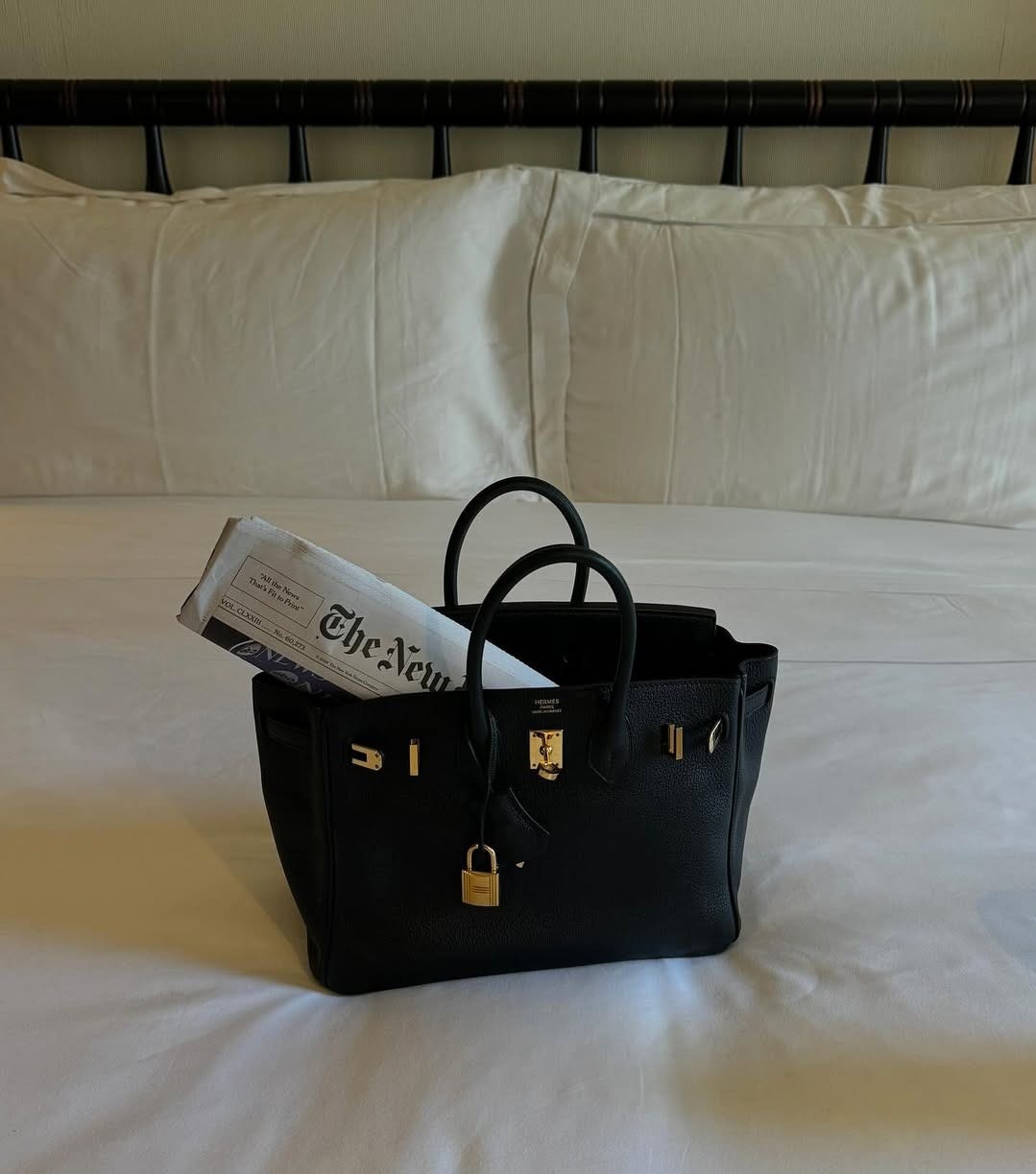 An Hermes bag with a newspaper popping out on a bed.