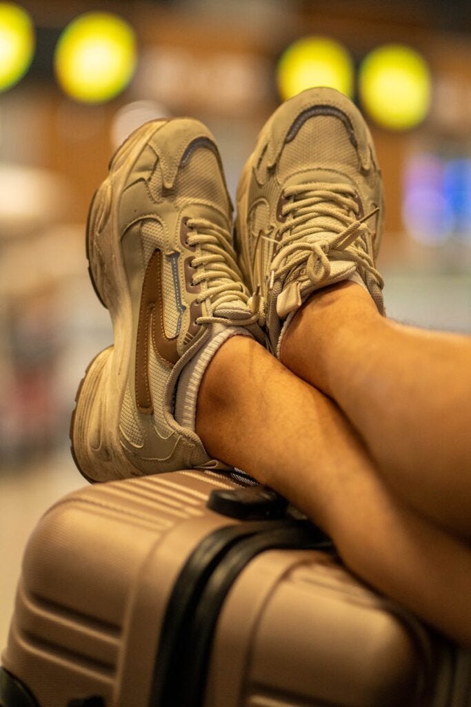 A person's feet resting on a suitcase at an airport