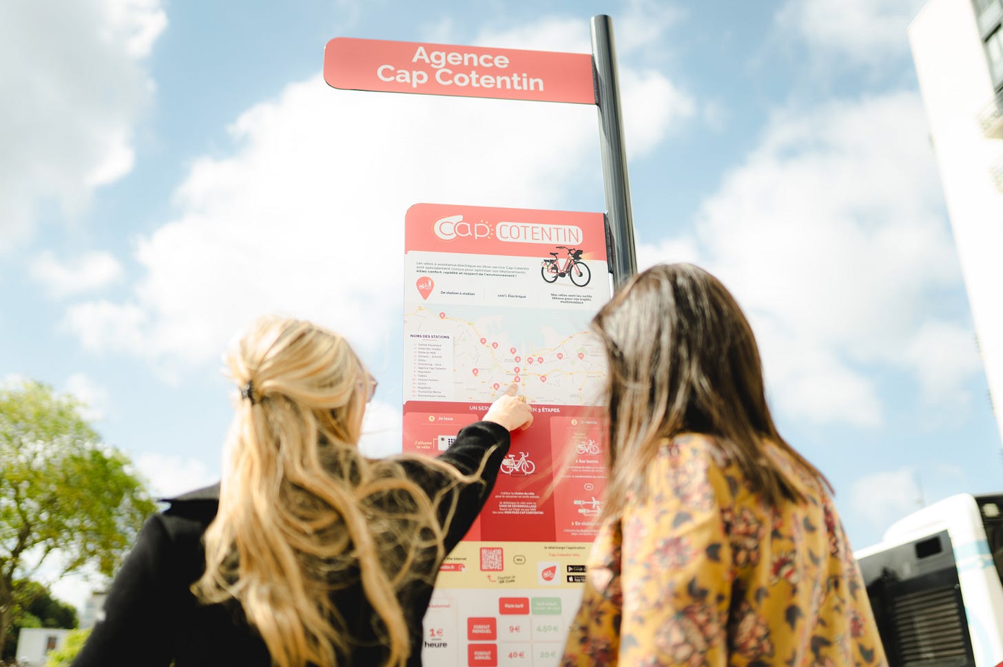 deux jeunes femmes devant un panneau de velo en libre service a cap cotentin