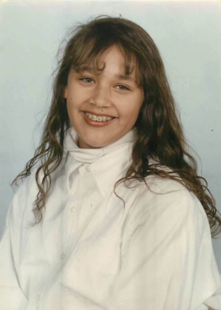 School portrait of young Rashida Jones at age 14, showing her with long dark hair, braces, and wearing a white turtleneck, smiling at the camera.