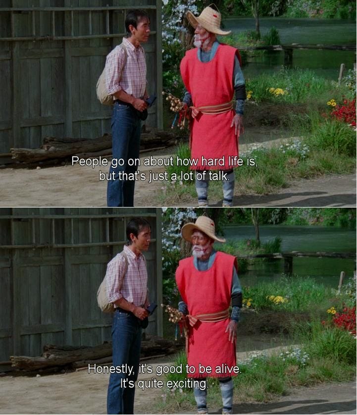 This may contain: an old man in a red vest and straw hat talking to another man with his hands on his hips