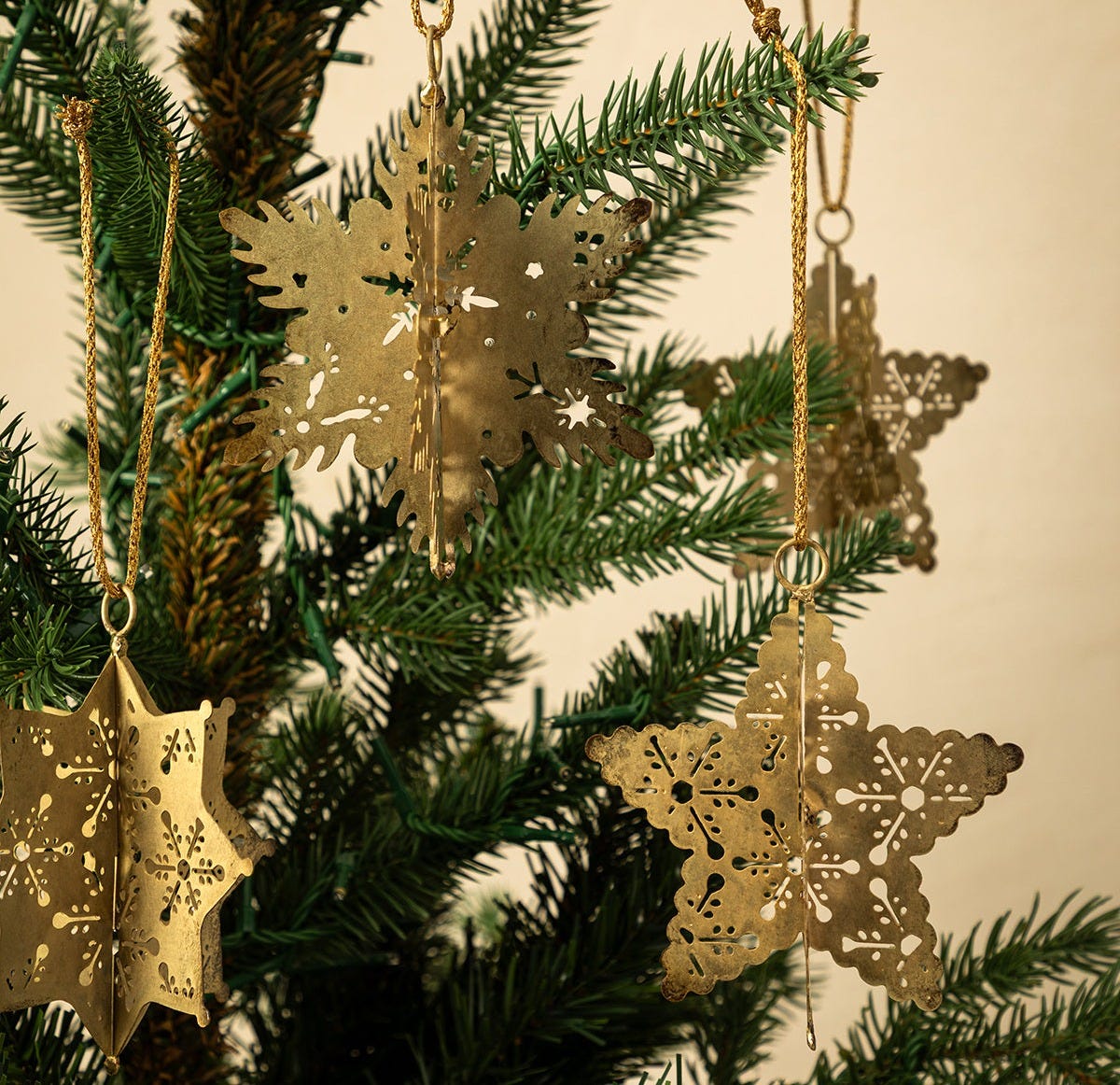 Close-up of Antique Gold Snowflake Ornaments (Set of 4) with intricate cut-out designs, hanging by gold strings among green pine branches—perfect for holiday decorating, by McGee & Co.