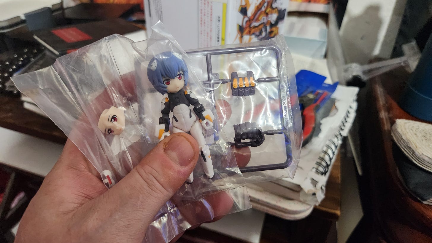 A packaged Rei Ayanami figure and the pieces of her mech's hands, all pre-painted