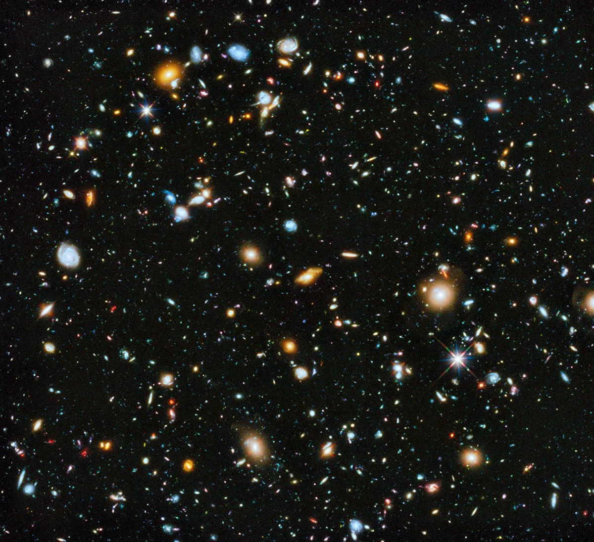 Field is filled with galaxies in colors of white, yellow, blue-white, and red; all on a black background. Field is filled with galaxies in colors of white, yellow, blue-white, and red; all on a black background.