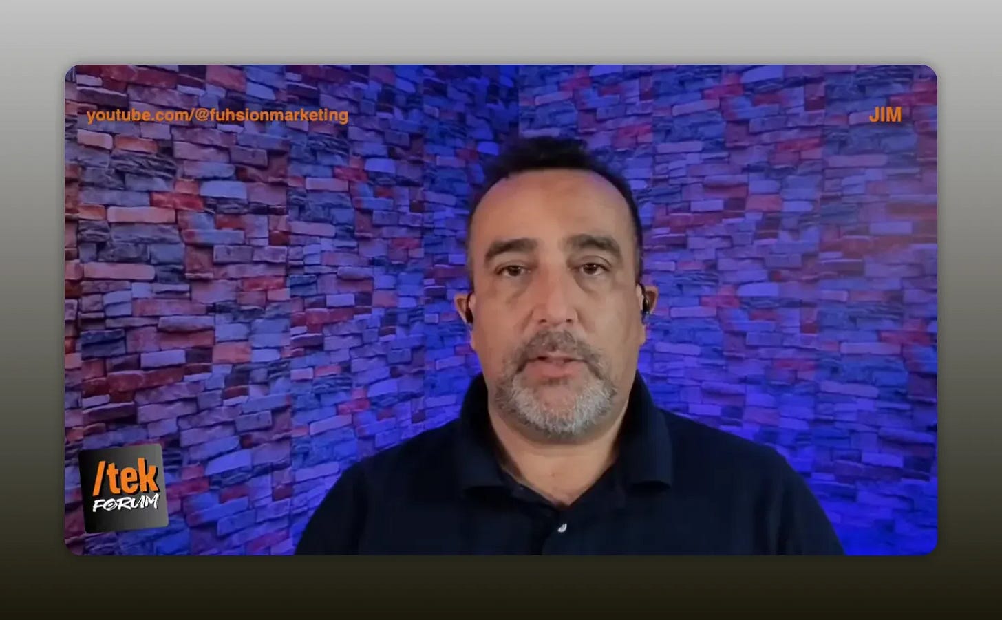 Centered, clear shot of presenter with blue-purple stone wall backdrop and visible logo