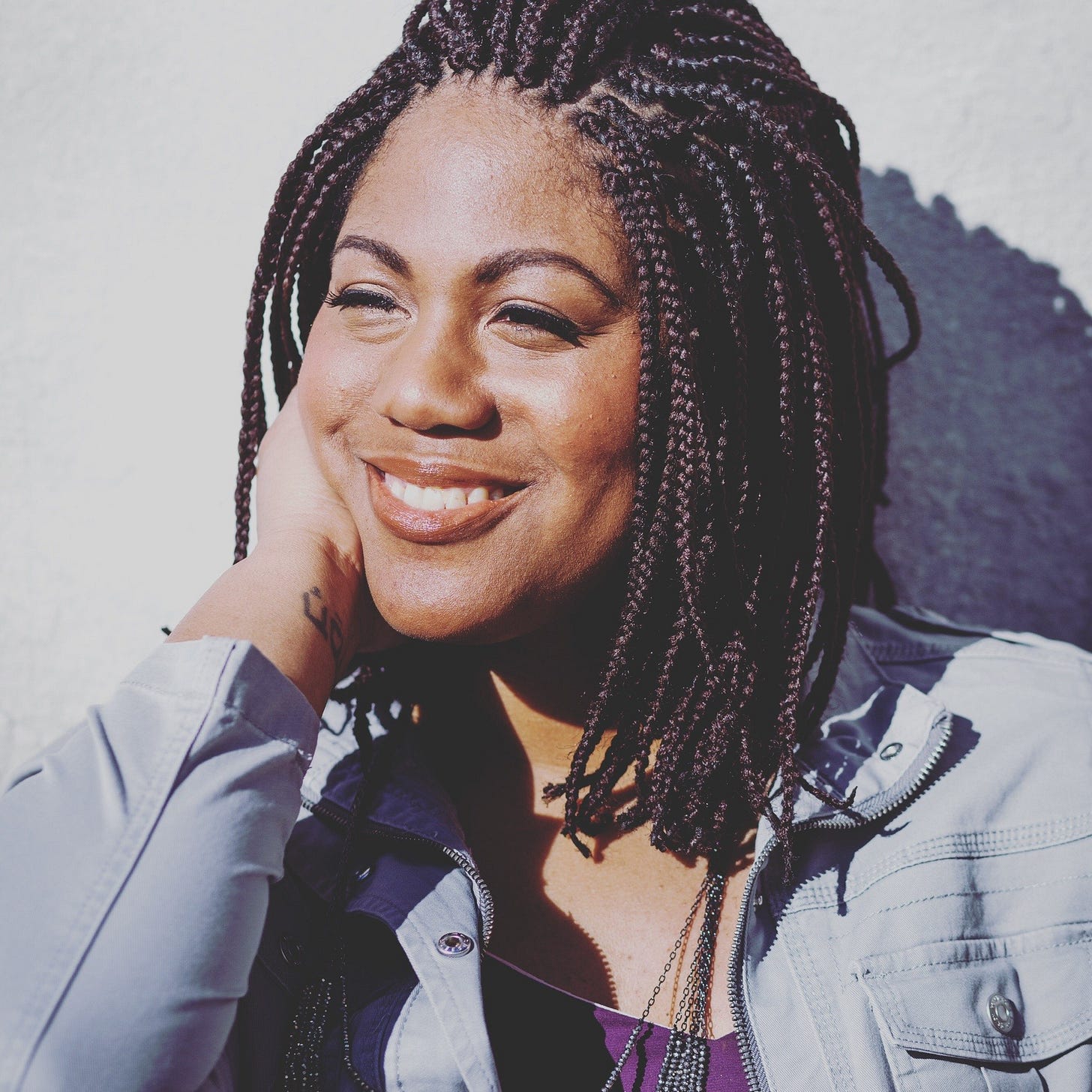 Austin, a Black woman with braids, rests her face on one hand and smiles while looking off into the distance