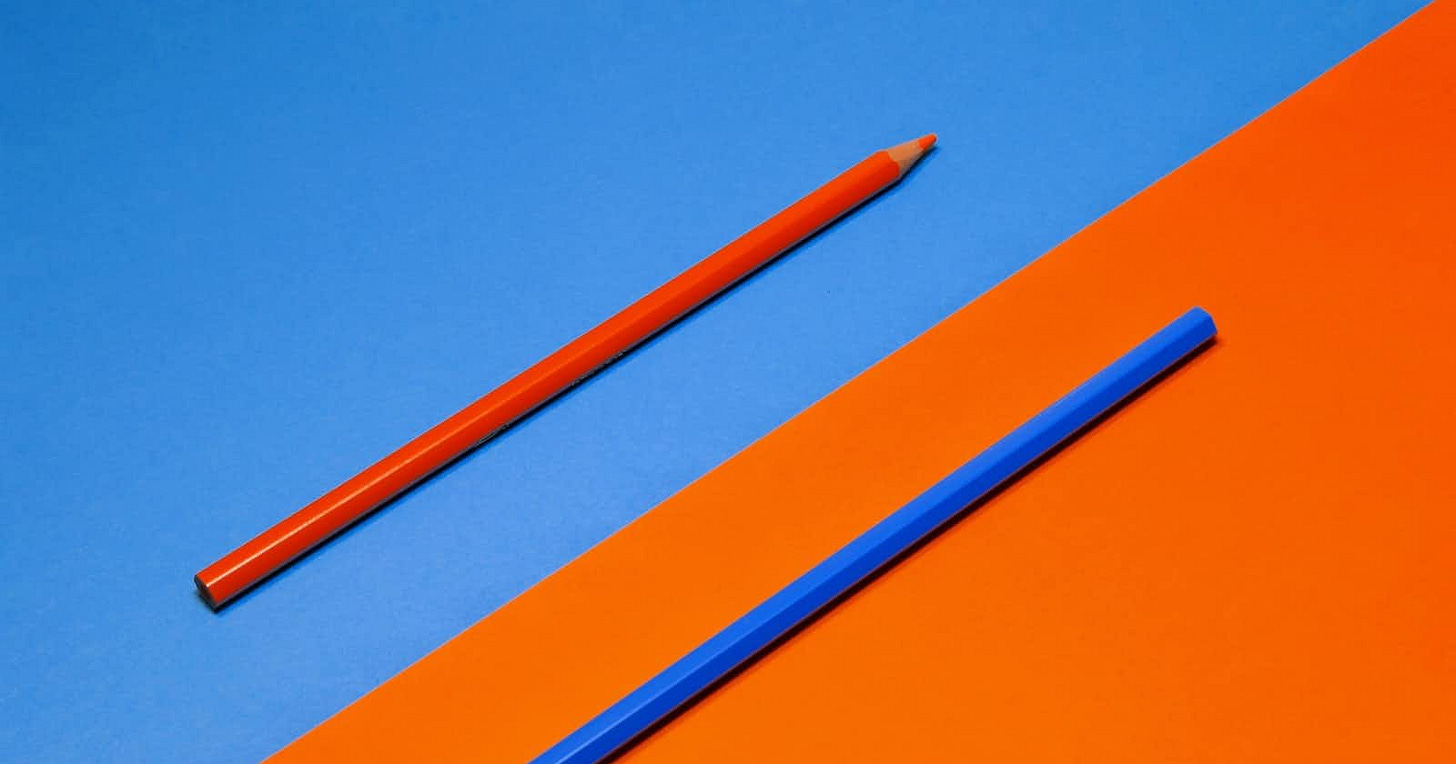 Two pencils on a divided background, with a blue pencil on the orange half and an orange pencil on the blue half.