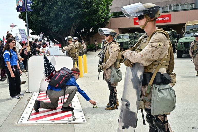 A man places a flower on the ground as armed US Marines guard the rear entrance to the Edward Royal Federal Building on June 14, 2025 in Los Angeles, after protesters participated in the "No Kings" demonstration.