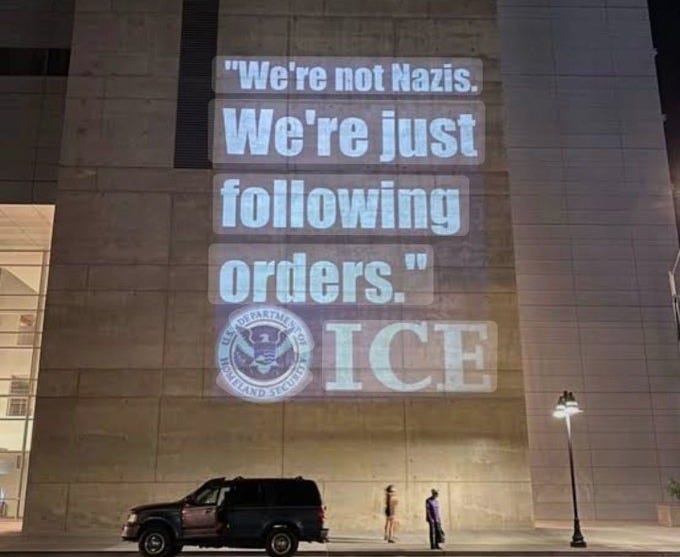 Projected words on the side of a building say "We're not Nazis. We're just following Orders."