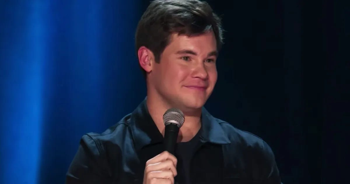 Adam Devine holding a mic on stage