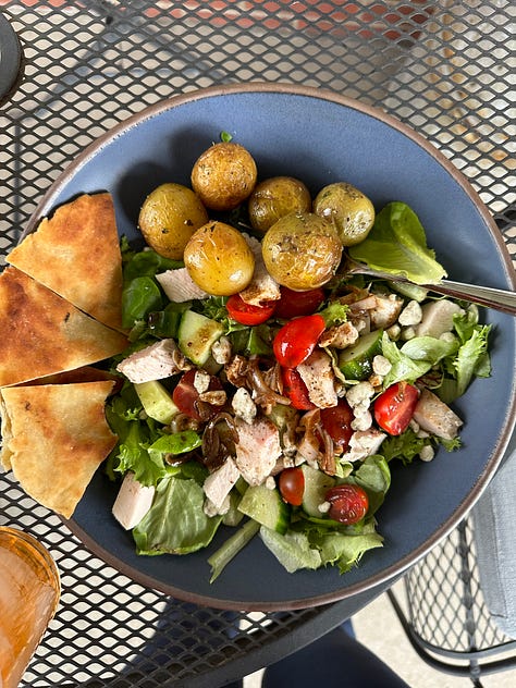 a blue bowl pictured with 3 different foods: salad, hummus, and pork tenderloin