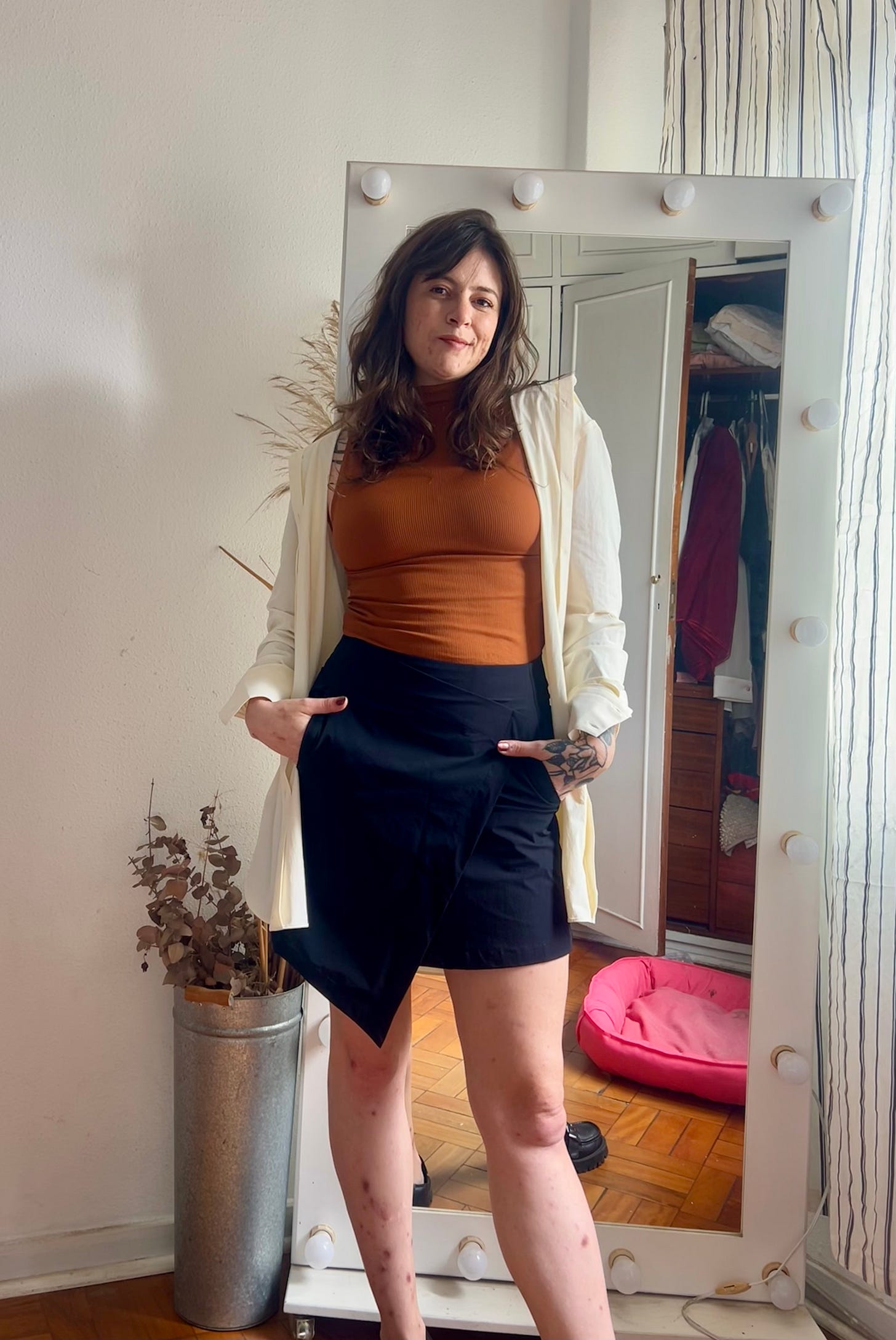 Euzinha de pé, com uma saia curta com recorte transpassado e assimétrico na frente, a mesma regata tijolo da foto anterior e, por cima, uma camisa aberta off-white