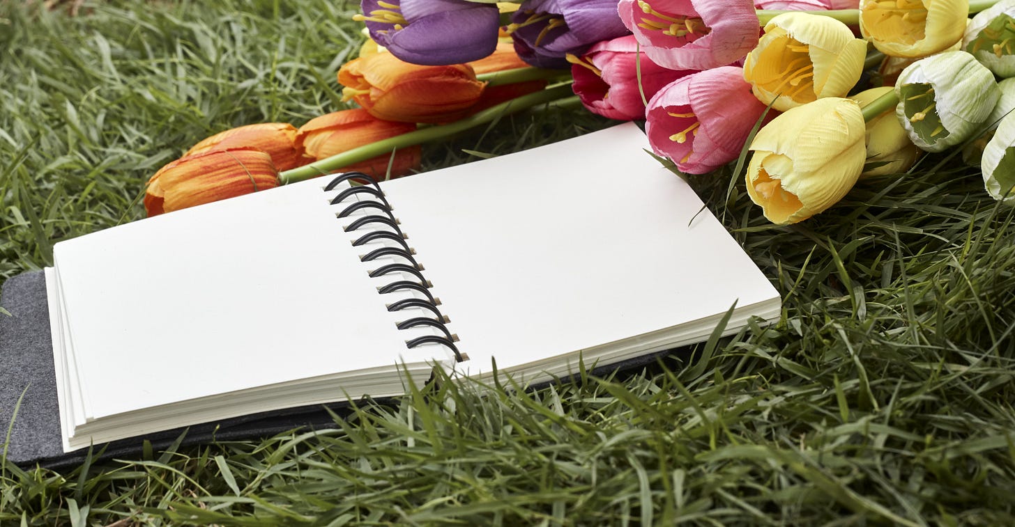 Open spiral notebook on grass with colorful tulips nearby.