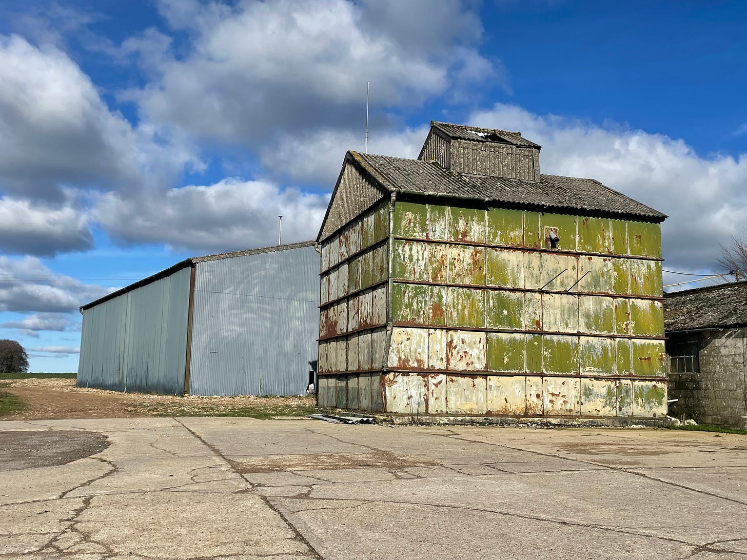 a grey building and a green-cream building on concrete with blue cloudy sky behind
