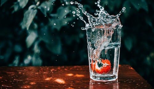 Free A vibrant strawberry splashes into a glass of water, captured mid-motion. Stock Photo Free A vibrant strawberry splashes into a glass of water, captured mid-motion. Stock Photo