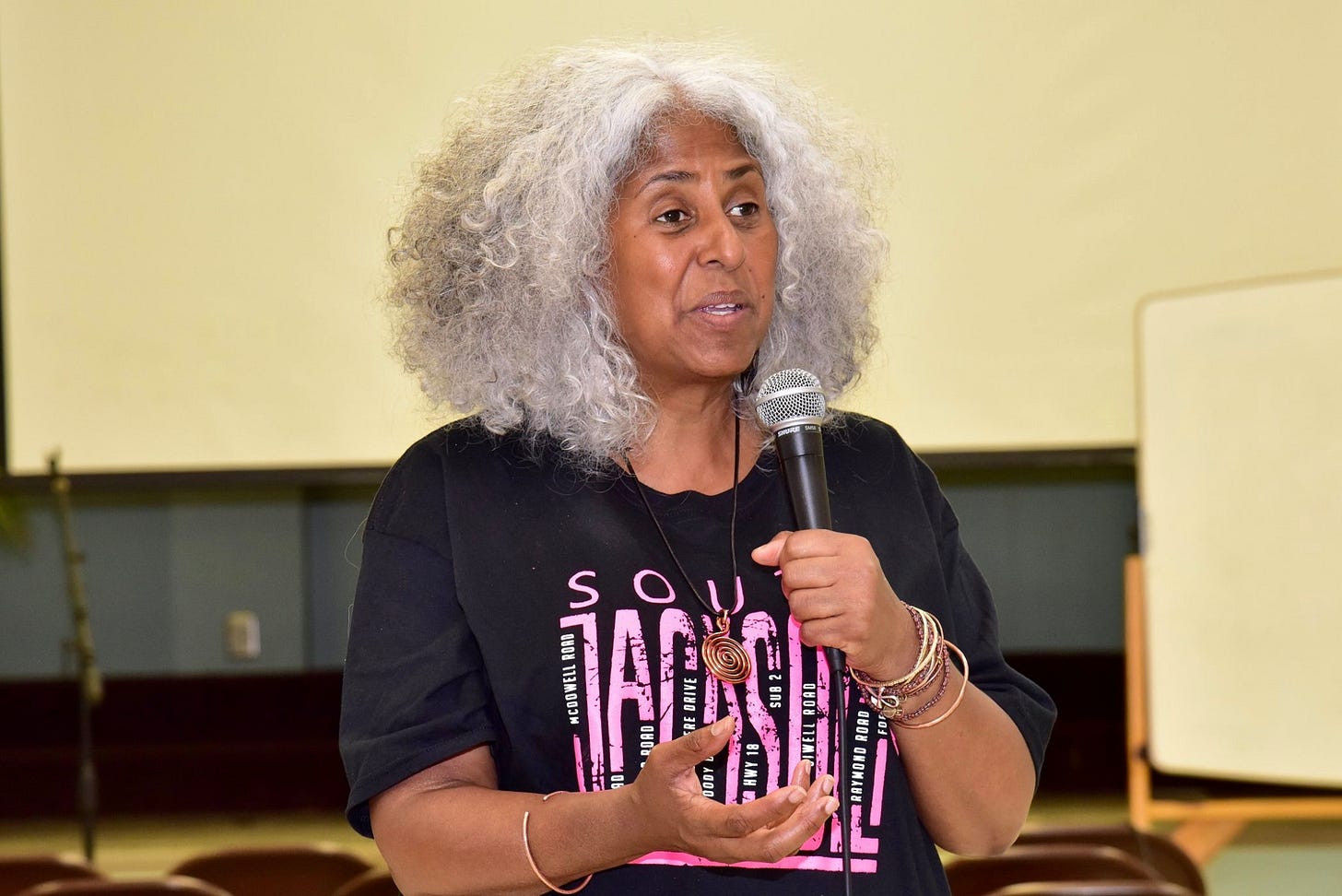 Makani wearing a black T-shirt with pink text that reads South Jackson. She is holding a microphone.