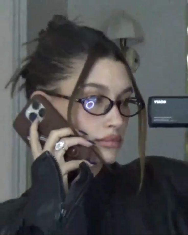 This may contain: a woman wearing glasses talking on a cell phone while standing in front of a mirror