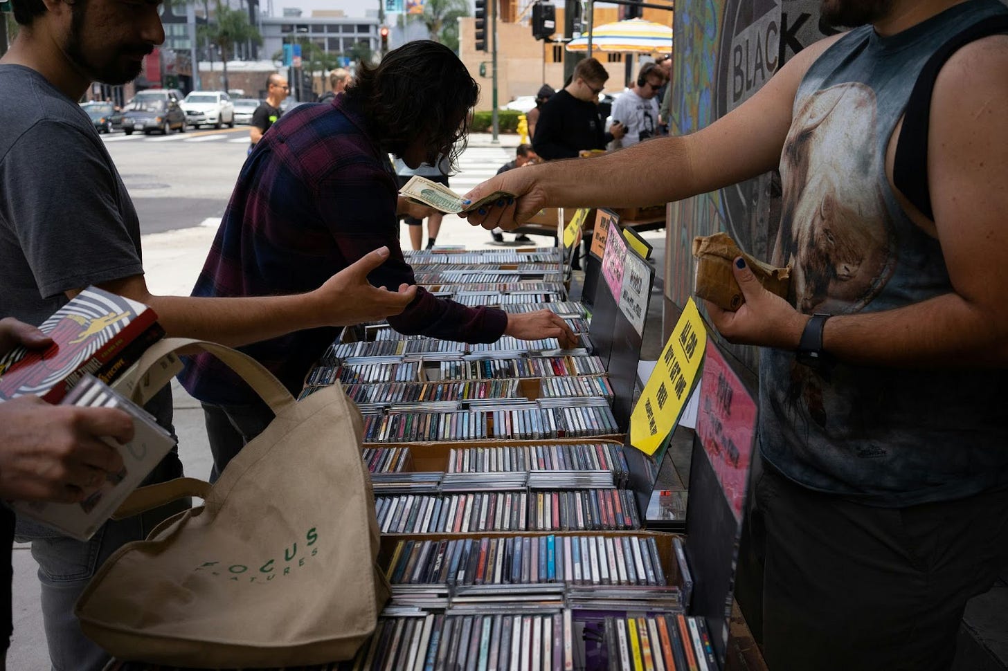 People browsing CDs for sale on a streetside market table People browsing CDs for sale on a streetside market table