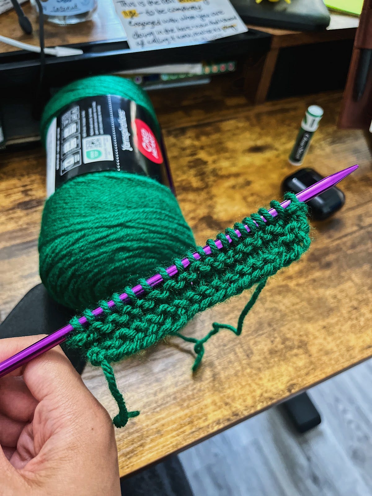 An emerald green skein of yarn with a knitting needle that has a skinny line of knits and a skinny line of purls on it. An emerald green skein of yarn with a knitting needle that has a skinny line of knits and a skinny line of purls on it.