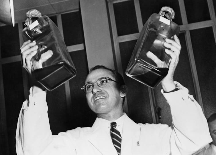 black-and-white image of man in white jacket holding up two bottles black-and-white image of man in white jacket holding up two bottles