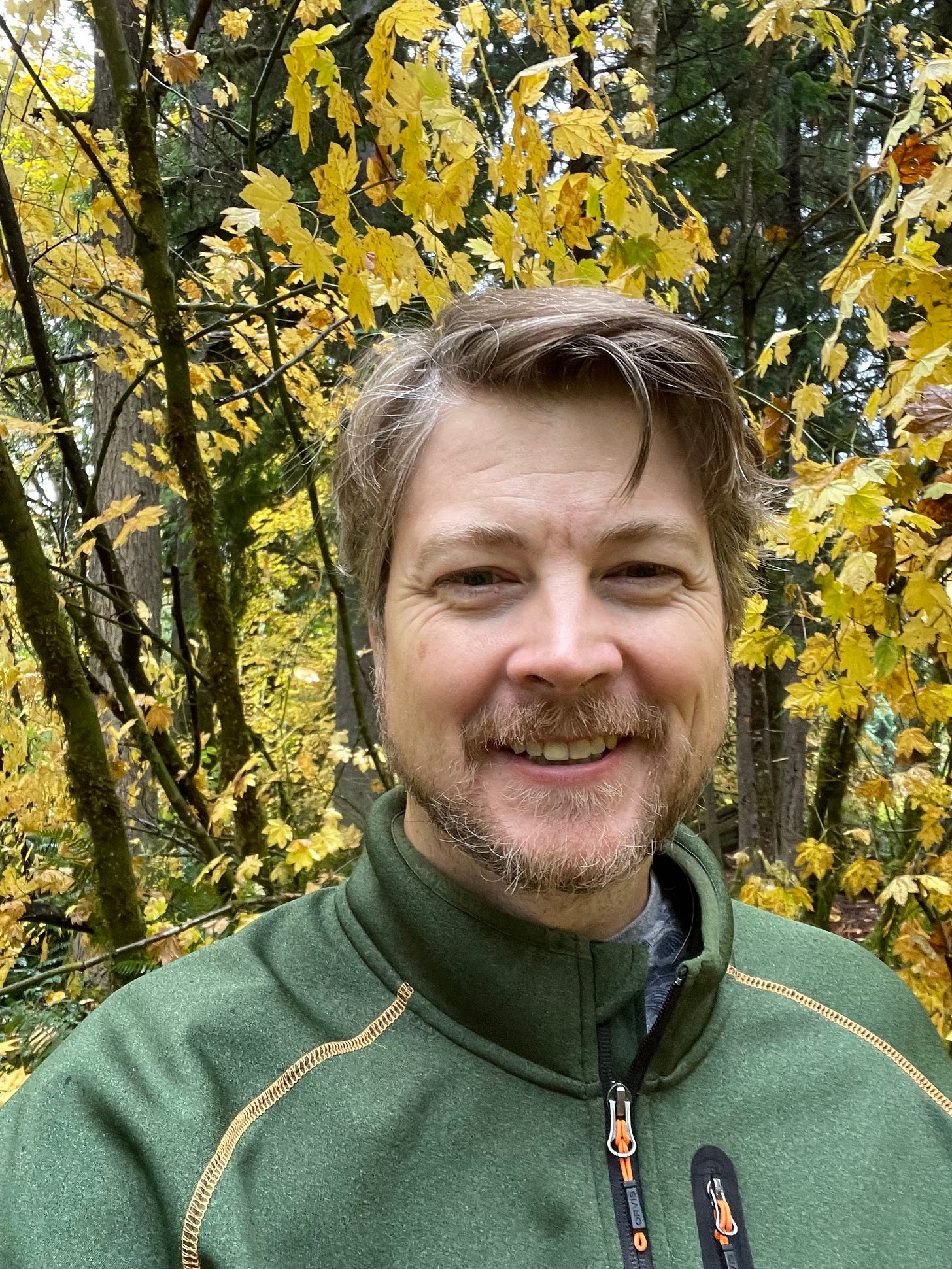 Author Dave Hill Jr. wearing a green jacket in front of a tree with yellow leaves